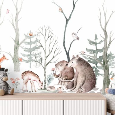 Zdjęcie przedstawia dziecięcy pokój z tapetą przedstawiającą akwarelową ilustrację zimowego lasu. Na tapecie widoczne są niedźwiedzie, lis, sarna, zając i ptaki. Przed tapetą stoi drewniana komoda, na której znajdują się pluszowe zabawki: żyrafa i zebra. W koszyku obok komody leżą pompony.