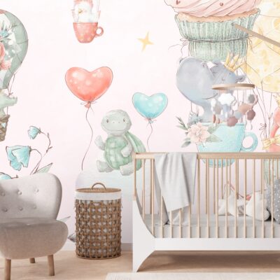 Różowa fototapeta akwarelowa z balonami i zwierzątkami na ścianie w pokoju dziecięcym. Na pierwszym planie łóżeczko dziecięce fotel oraz wilkinowy kosz.