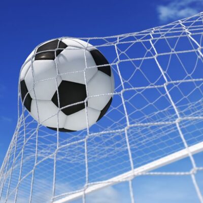 Fototapeta dla chłopca przedstawiająca piłkę nożną wpadającą do siatki bramki na tle błekitnego nieba