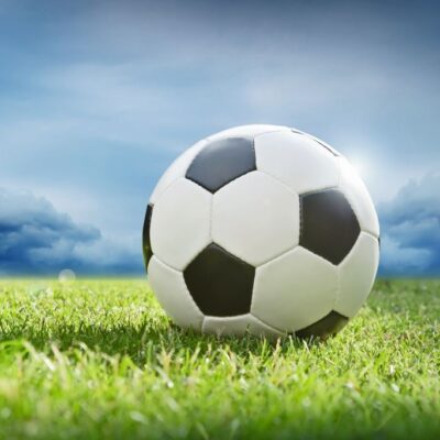 Fototapeta piłka nożna leżąca na murawie na tle zachmurzonego nieba