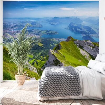 obrazek przedstawia nowoczesną sypialnię z białym łóżkiem i dużym kwiatem . Na wprost na ścianie fototapeta przedstawiająca widok z górskiego szczytu na panoramę gór