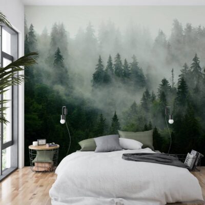 Fototapeta ścienna przedstawiająca mglisty las iglasty w ciemnozielonej tonacji, zamontowana za łóżkiem w jasnej, nowoczesnej sypialni w stylu skandynawskim.