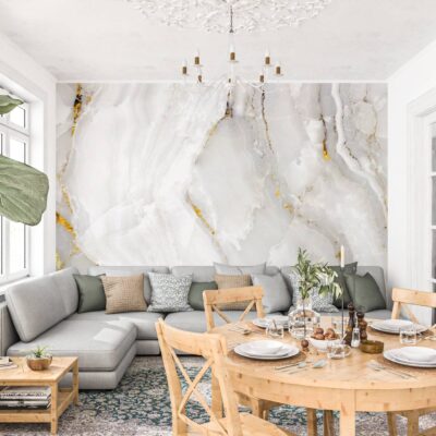 Fototapeta z motywem białego i jasnoszarego marmuru z eleganckimi, złotymi użyleniami w jasnym salonie. Wielkoformatowa dekoracja ścienna imitująca naturalny kamień, umieszczona za szarą sofą w nowoczesnej jadalni z drewnianymi meblami. Grafika o luksusowym charakterze, dodająca wnętrzu blasku i prestiżu.