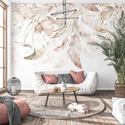 Jasny, nowoczesny salon w stylu boho z fototapetą przedstawiającą wielkoformatowe, akwarelowe liście i pióra w odcieniach beżu, kremu i delikatnego brązu. Na tle ściany stoi biała sofa z różowymi poduszkami, drewniany stolik kawowy oraz duża roślina doniczkowa, tworząc przytulną i elegancką aranżację.