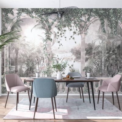 Nowoczesna jadalnia z fototapetą przedstawiającą tropikalny las we mgle. Wzór w stonowanych kolorach szałwiowej zieleni i szarości ukazuje palmy oraz zwisające pnącza, tworząc efekt głębi na ścianie. Na tle fototapety stoi ciemny drewniany stół z eleganckimi krzesłami w kolorze pudrowego różu i błękitu, a całość dopełnia duża roślina doniczkowa po lewej stronie.
