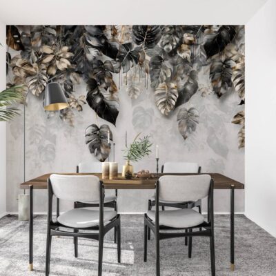 obrazek przedstawia Nowoczesną jadalnię z efektowną fototapetą przedstawiającą kaskadę dużych liści monstery. Wzór łączy w sobie głęboką czerń, eleganckie złoto (ochrę) oraz delikatne, szare kontury liści na jasnym tle o strukturze betonu. Przed ścianą znajduje się minimalistyczny drewniany stół z jasnoszarymi krzesłami na czarnych nogach, co tworzy spójną i luksusową aranżację.
