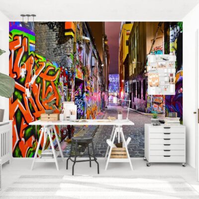 Aranżacja nowoczesnego pokoju z biurkiem i fototapetą na ścianie, przedstawiającą perspektywę wąskiej miejskiej uliczki pokrytej wielobarwnym graffiti i neonami w stylu street art.