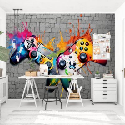 Nowoczesny pokój nastolatka z białym biurkiem na kozłach i komodą, udekorowany dużą fototapetą z motywem dwóch padów do konsoli z kolorowymi efektami graffiti na tle szarej ściany z cegły. W jasnym wnętrzu widoczna jest duża roślina doniczkowa i białe drzwi.
