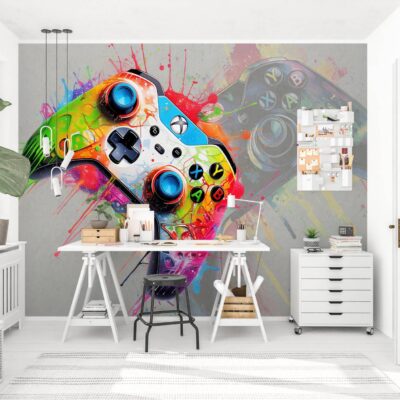 Jasne biuro domowe z białym biurkiem na kozłach, czarnym taboretem i dużą fototapetą przedstawiającą kolorowy kontroler do gry z dynamicznymi rozbryzgami farby graffiti na szarym tle. W pokoju widoczna jest duża zielona roślina, biała komoda oraz stylowy organizer ścienny.