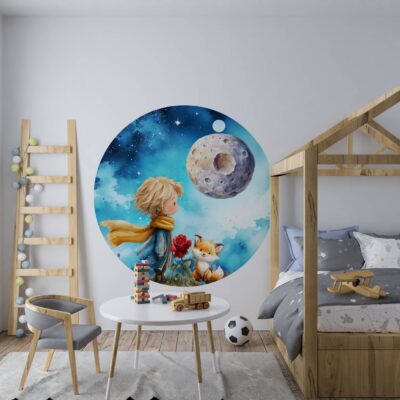 Aranżacja nowoczesnego pokoju dziecięcego z okrągłą naklejką tkaninową na ścianie. Akwarelowa grafika przedstawia Małego Księcia z rozwianym szalikiem, lisa oraz różę w szklanym kloszu na tle księżyca i granatowego nieba. Wnętrze wyposażone w drewniane łóżko w kształcie domku, biały stolik i drabinę dekoracyjną.